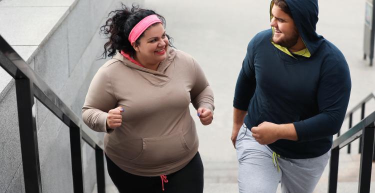 A woman and a man out jogging. They are climbing a flight of concrete steps and smiling at each other.