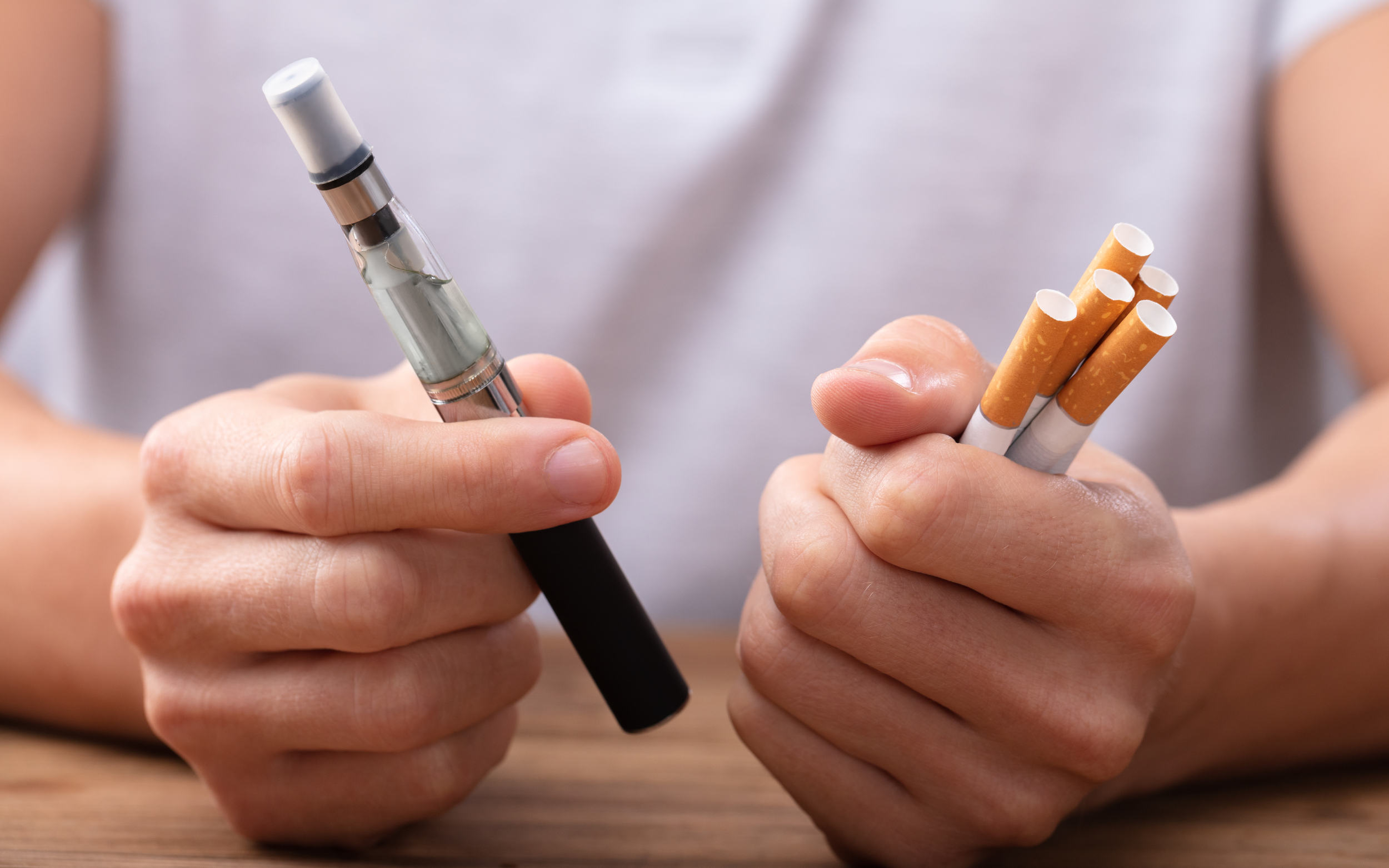 A person holding cigarettes in one hand and a vape in the other