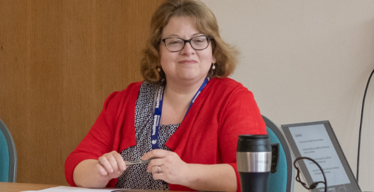 Philippa Brice wearing a red top, sat at a table, chairing a workshop