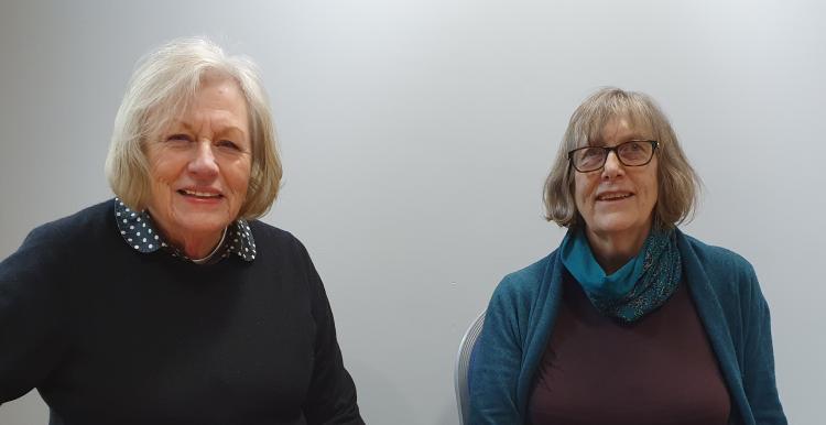 Ann Green and Frances Dewhurst sitting at a table together and smiling at the camera