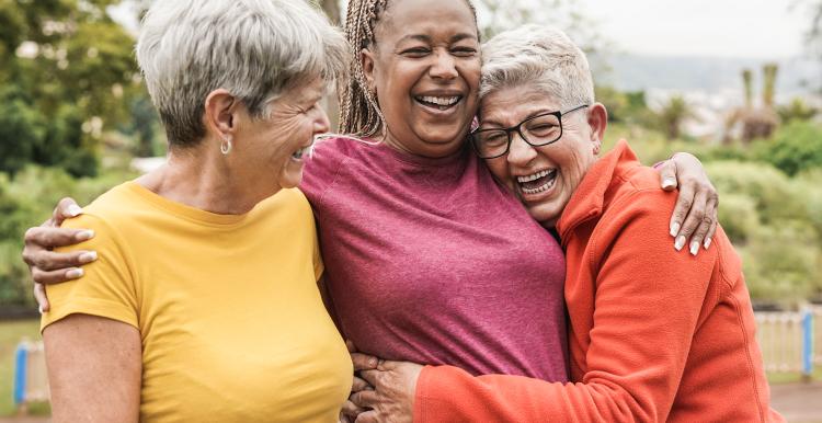 Three women outdoors. They are hugging each other and laughing.