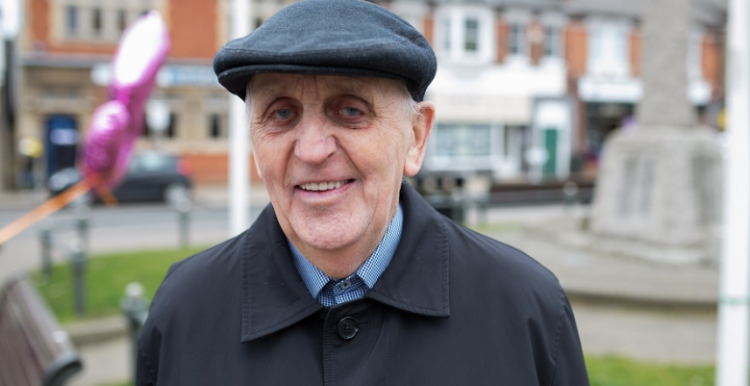 older man in a flat cap smiling at camera