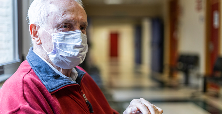 man wearing face covering waits in hospital corridor