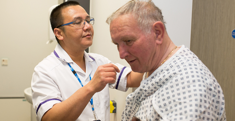 Picture shows man in hospital gown and an NHS radiographer preparing him for treatment
