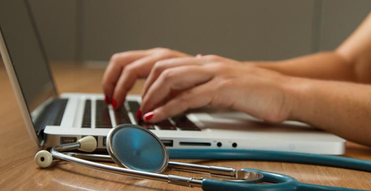 woman typing into laptop next to stethoscope