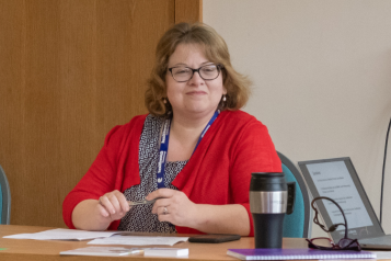 Philippa Brice wearing a red top, sat at a table, chairing a workshop