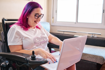 A smiling woman sat in a wheelchair with a laptop on her lap.