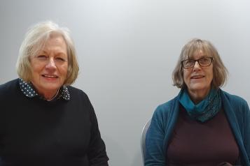 Ann Green and Frances Dewhurst sitting at a table together and smiling at the camera