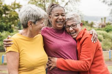 Three women outdoors. They are hugging each other and laughing.