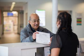 Man hands piece of paper to medical receptionist