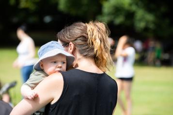 A mother holding a baby. She is standing in park.