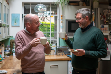 Two men standing in a kitchen having a cup of tea