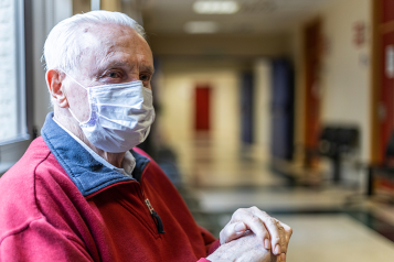 man wearing face covering waits in hospital corridor