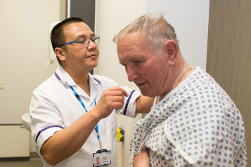 Picture shows man in hospital gown and an NHS radiographer preparing him for treatment