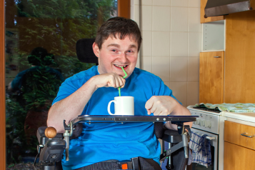 Picture shows man in wheelchair in his kitchen having a drink using a straw