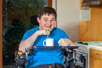Disabled man in a wheelchair in his kitchen drinking from a cup with a straw 