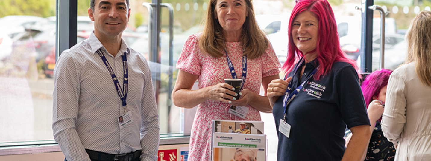 Members of Healthwatch Cambridgeshire and Peterborough staff smiling and standing by a desk with Healthwatch reports and leaflets on it
