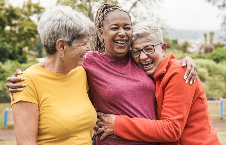Three women outdoors. They are hugging each other and laughing.